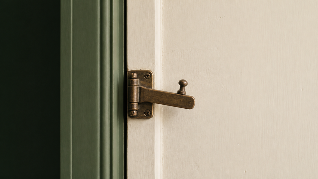 An antique brass latch on a cream door with a sage green frame