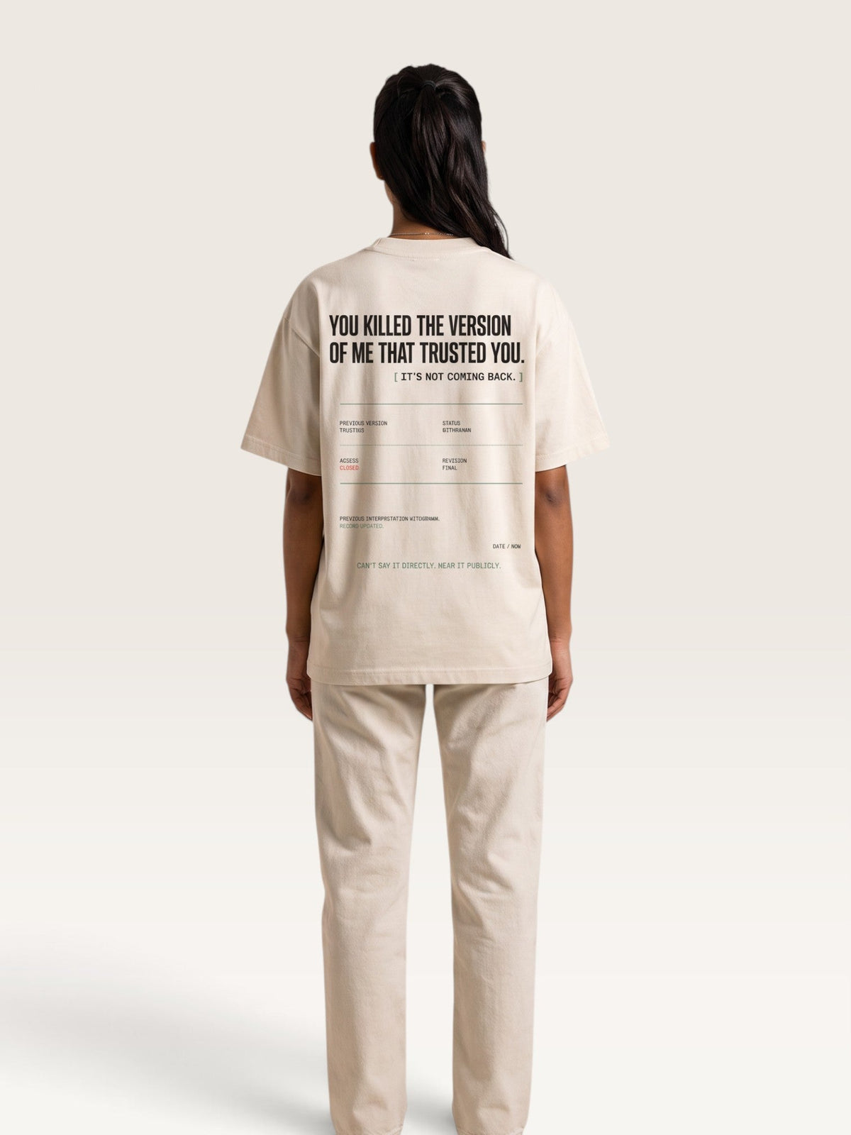 Mild Apricot - A model shown from the back wearing a beige oversized t-shirt and matching beige trousers. The t-shirt features black text on the back reading 'YOU KILLED THE VERSION OF ME THAT TRUSTED YOU.