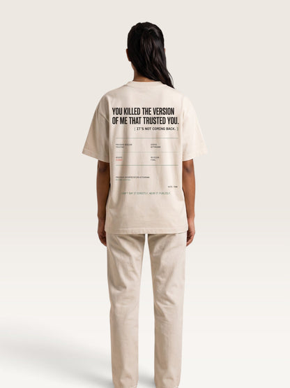 Mild Apricot - A model shown from the back wearing a beige oversized t-shirt and matching beige trousers. The t-shirt features black text on the back reading 'YOU KILLED THE VERSION OF ME THAT TRUSTED YOU.