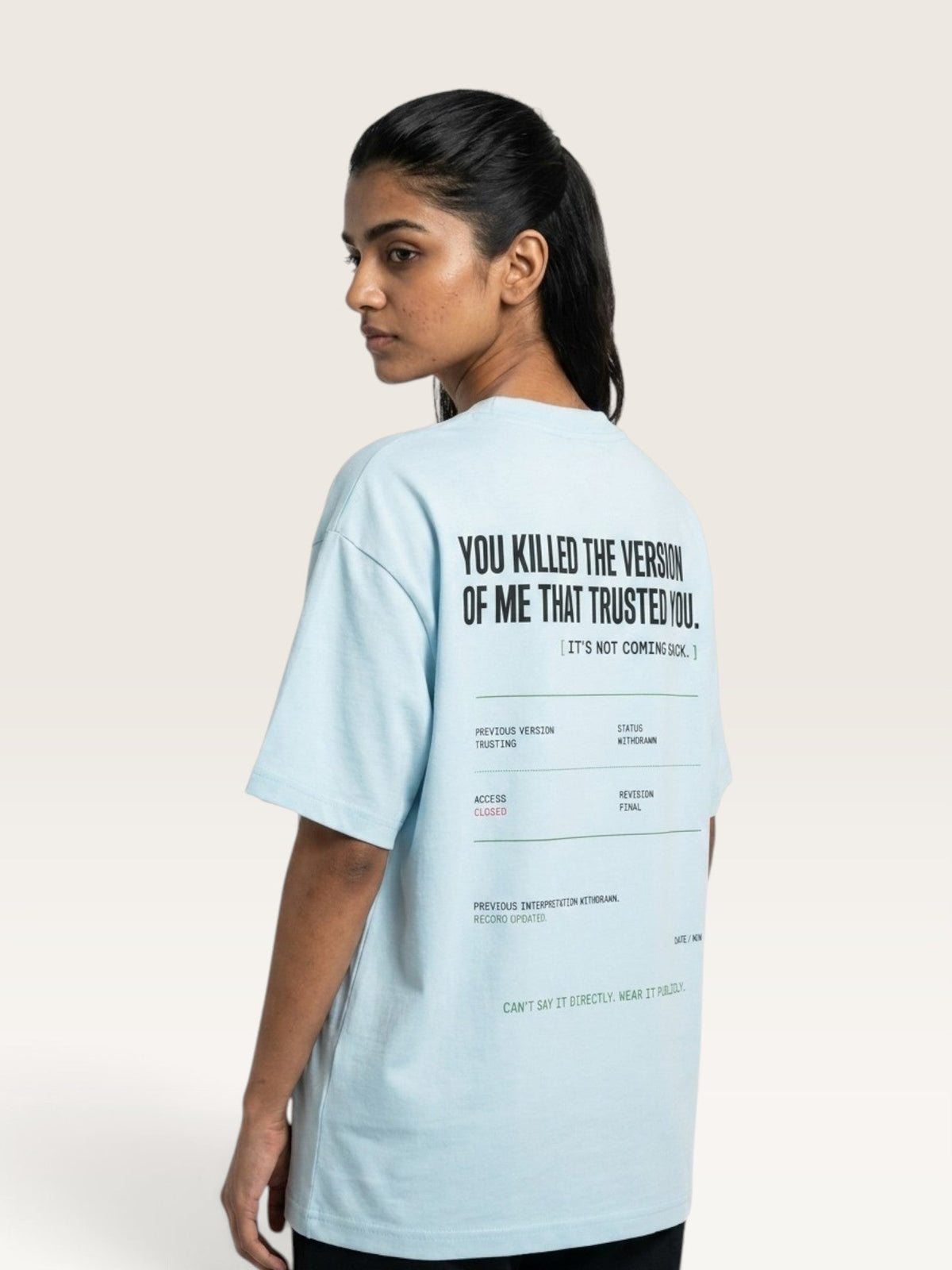 Sky Blue A woman shown from the back wearing a light blue oversized T-shirt with black printed text on the back, photographed against a plain light beige studio background.