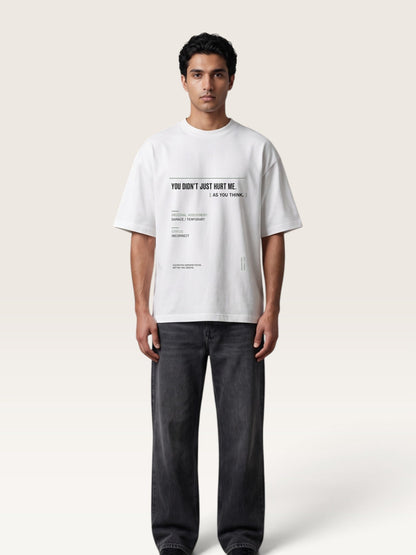 White - A man wearing a white oversized graphic T-shirt with black text and dark gray jeans, standing against a plain light beige studio background.