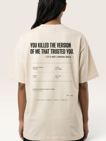 Mild Apricot - person shown from the back wearing a light beige oversized T-shirt with black text and a minimalist typographic graphic on the back, against a plain light beige studio background.