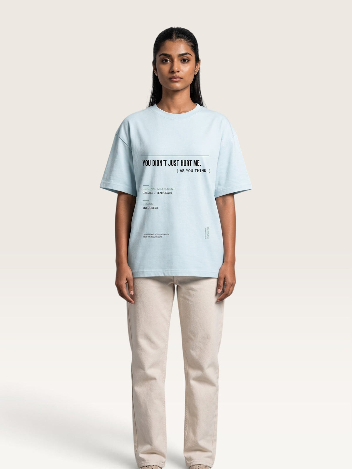 Sky Blue - A model stands against a light beige studio background wearing an oversized light blue graphic T-shirt and cream-colored trousers. The T-shirt features black printed text on the chest reading 'YOU DON'T JUST HURT ME.