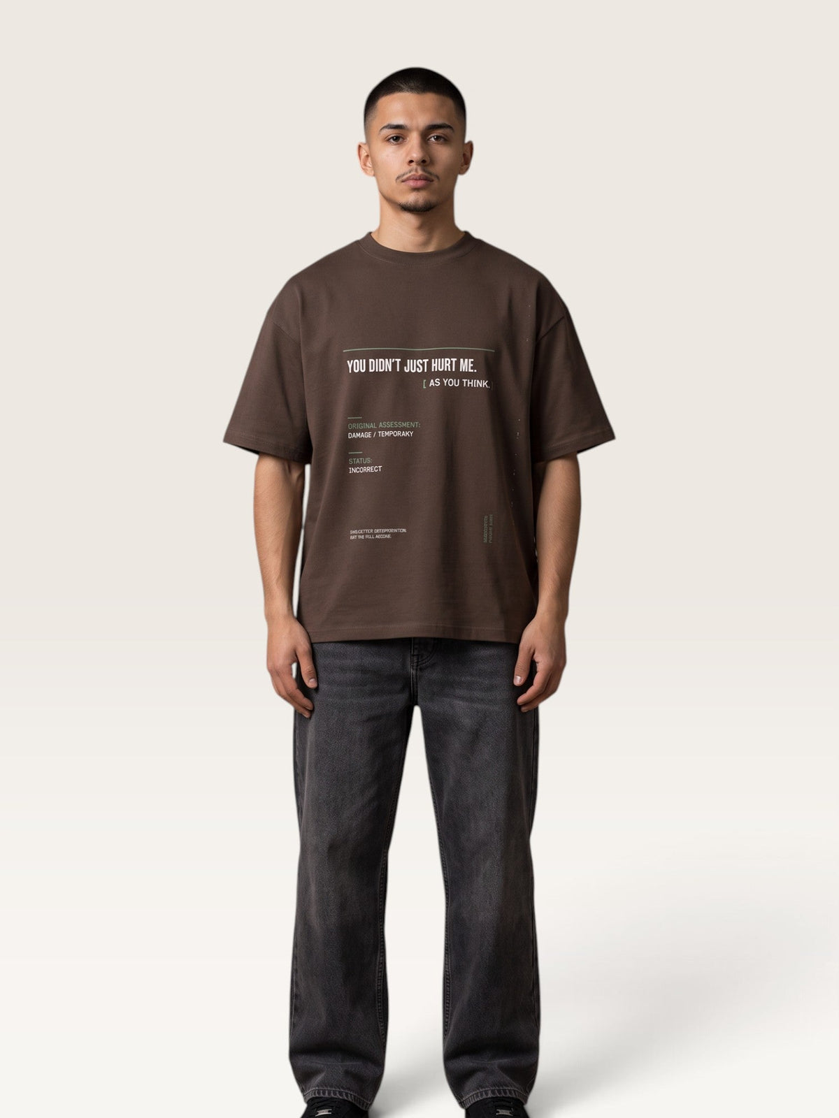 Coffee - A man wearing an oversized dark brown graphic t-shirt and dark gray jeans, standing against a light beige studio background.