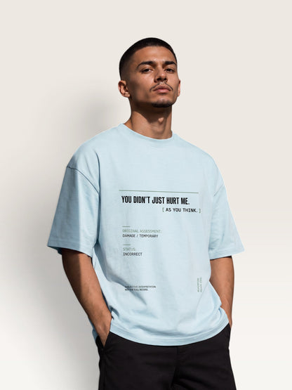 Sky Blue - A man wearing a light blue oversized graphic t-shirt with black text on the front, paired with black pants, standing against a plain off-white background.
