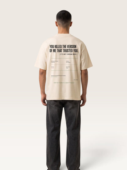 Mild Apricot - A man viewed from behind wearing a cream-colored t-shirt with black text on the back and dark gray jeans, standing against a light beige studio background.