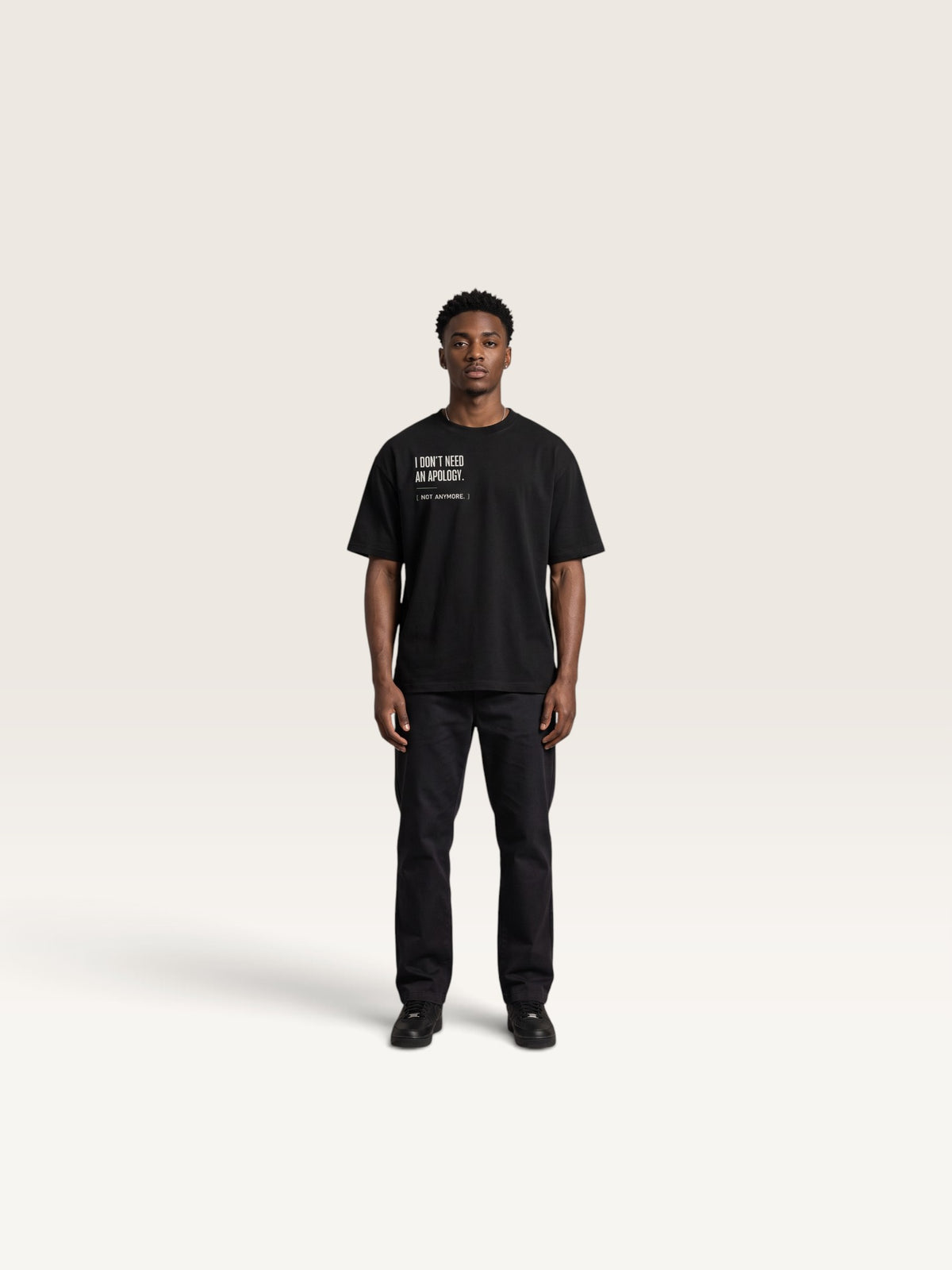 Black WEARCAPTION model wearing a black heavyweight cotton oversized t-shirt with white I DON'T NEED AN APOLOGY text print